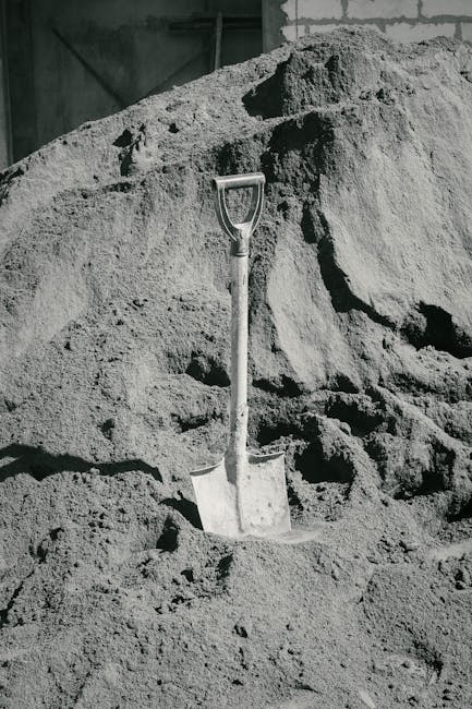 A solitary shovel upright in a massive sand pile, representing construction and labor.